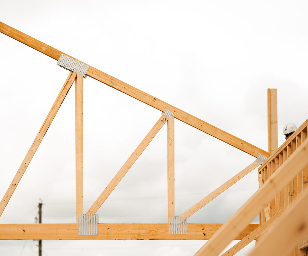 A man stands on a rooftop, helping set a large truss into place